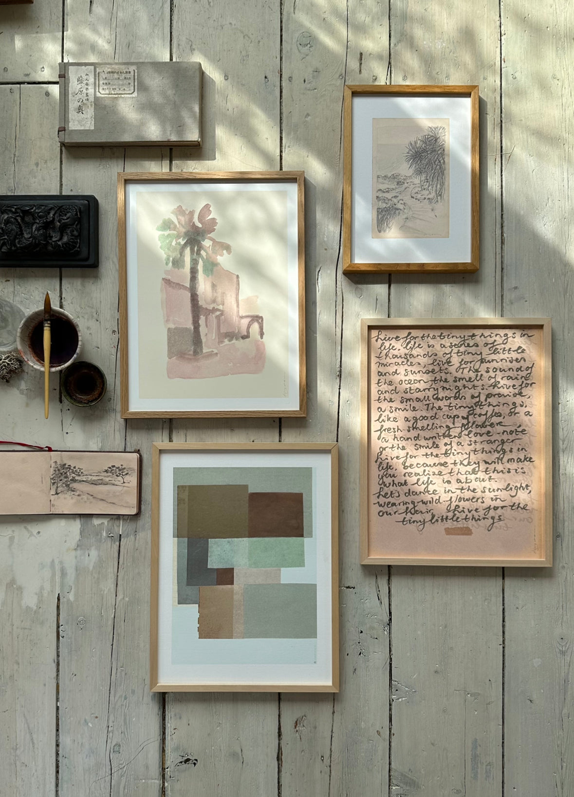 Collection of framed abstract, figurative, and botanical artworks including handwritten poetic text laid out on rustic wooden floor