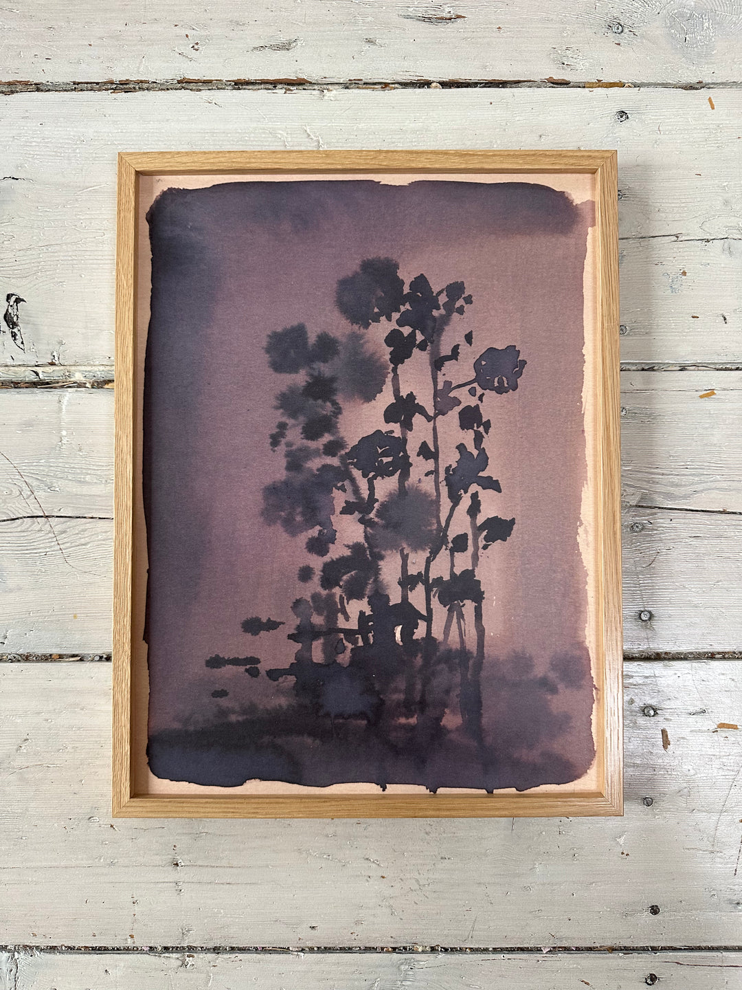 Framed in brown wooden frame, dark floral painting on a rustic white floor.