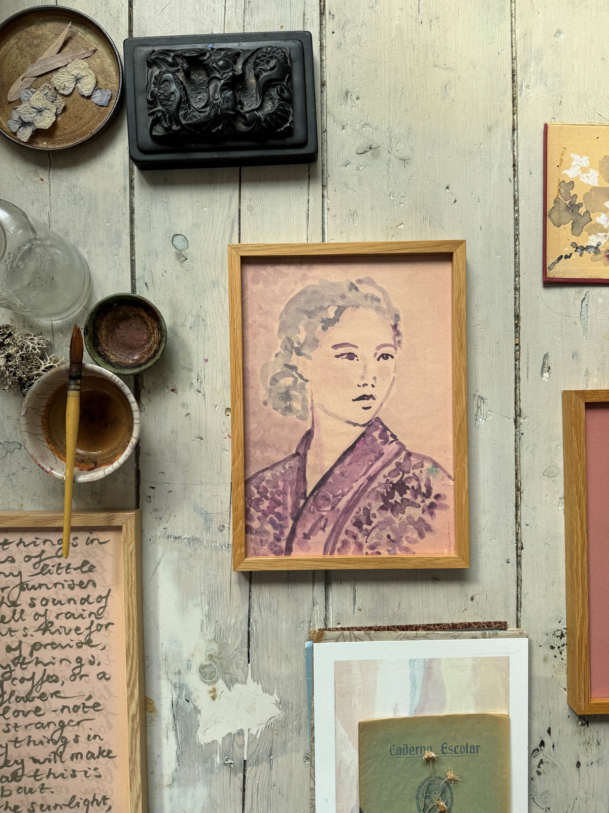 Framed portrait of woman in floral kimono hanging on rustic wooden wall with sunlight and nearby art pieces.