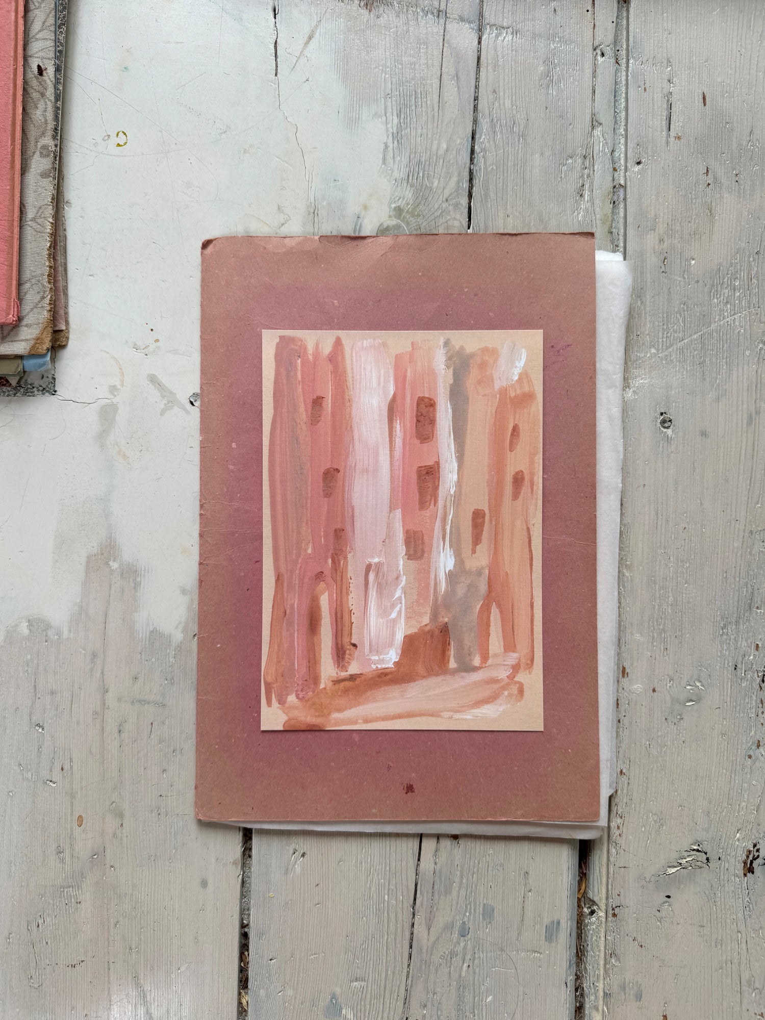 Small abstract cityscape watercolor on reddish board on worn wooden floor.
