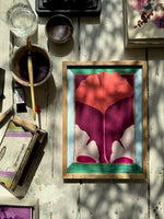 Framed abstract floral art with red and purple tones on wooden floor surrounded by paintbrush and art supplies