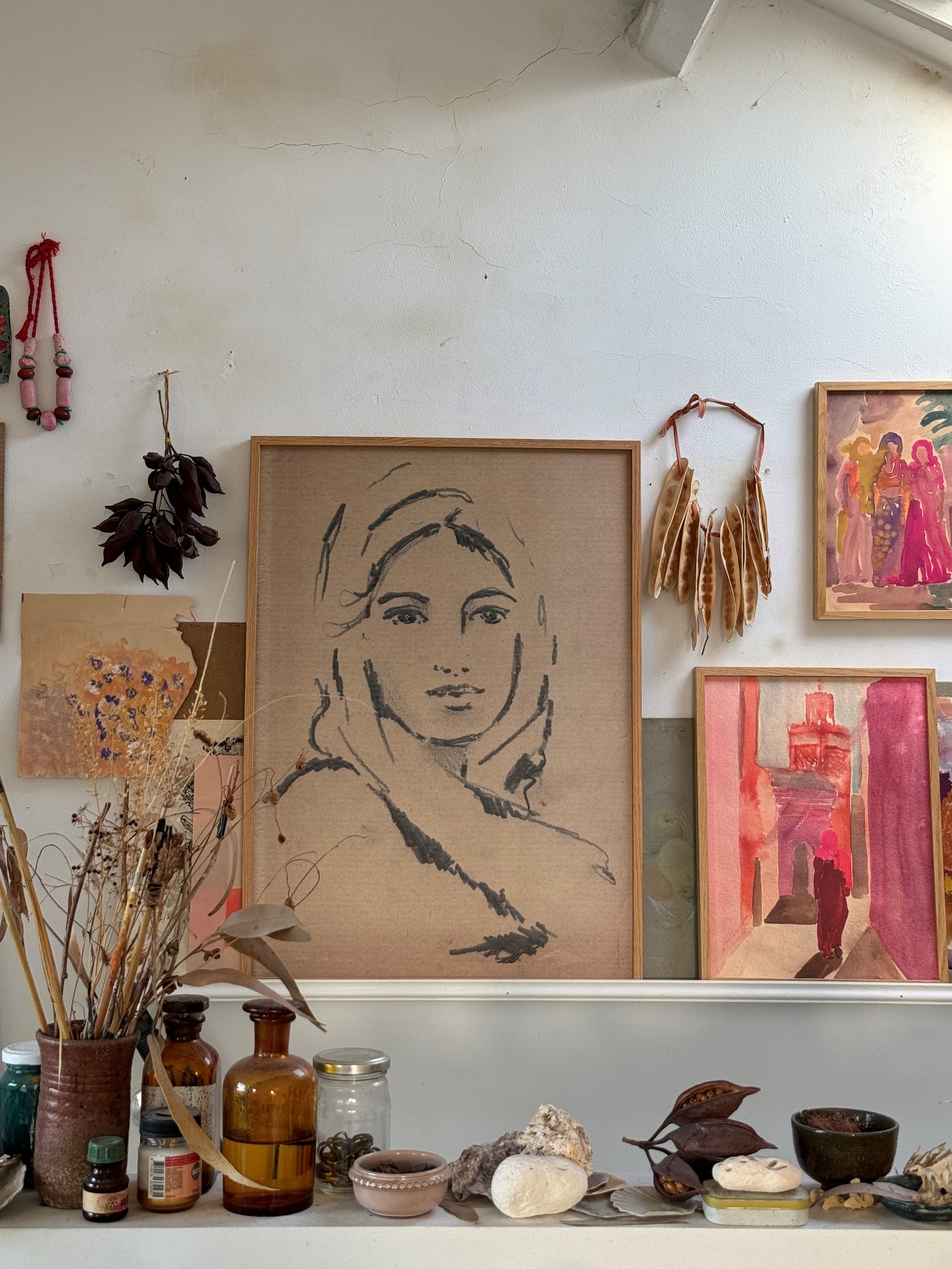 Framed pencil sketch of a lady against a white attic wall along with other colorful framed paintings.