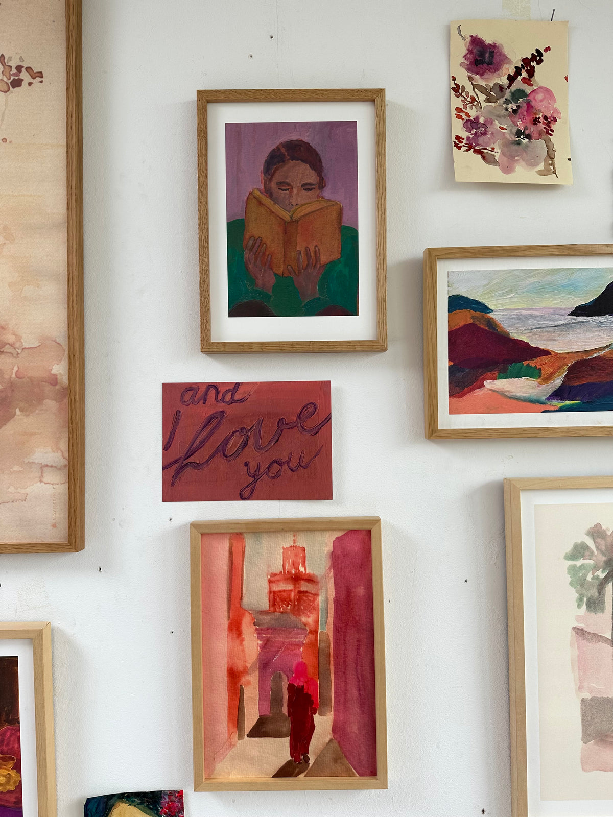 Gallery-style wall with multiple framed paintings including a reading figure, floral art, and colorful landscapes.