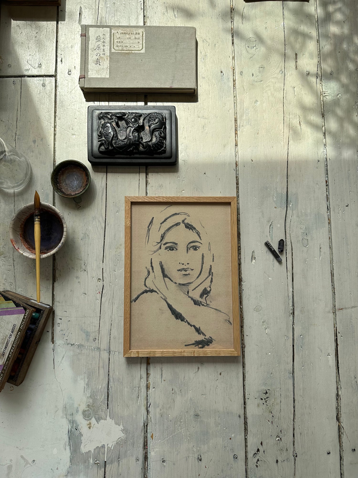 Framed pencil sketch of a lady on a white wooden rustic floor with paint brush nearby