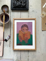 Framed painting of person reading orange book, purple background, on rustic wooden floor with paintbrush and art supplies nearby.
