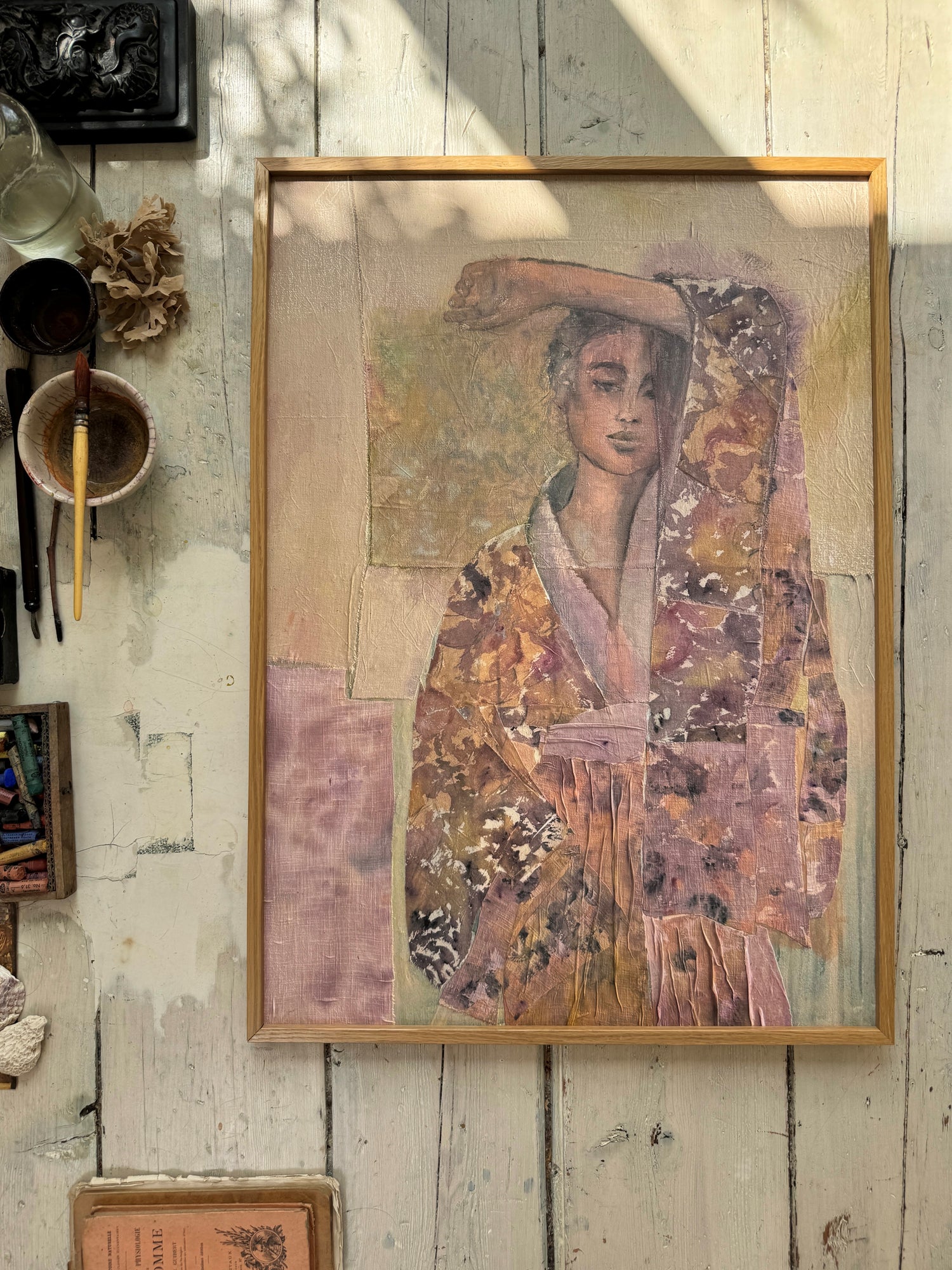 Framed watercolor painting of a woman in a floral kimono with hand raised over her forehead on rustic white wooden floor with art tools nearby