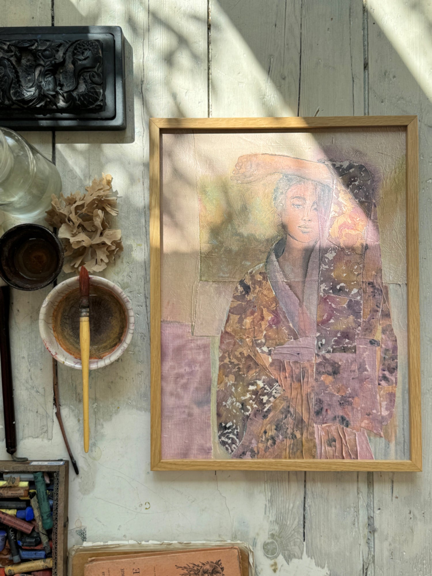 Framed watercolor painting of a woman in a floral kimono with hand raised over her forehead on rustic white wooden floor with art tools nearby