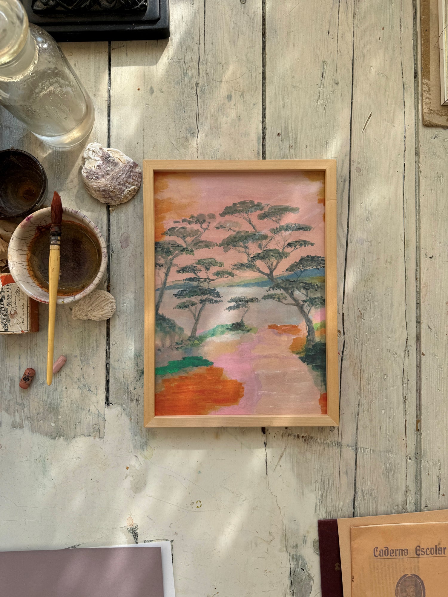 Framed abstract tree painting on wooden floor with art supplies and shells around.