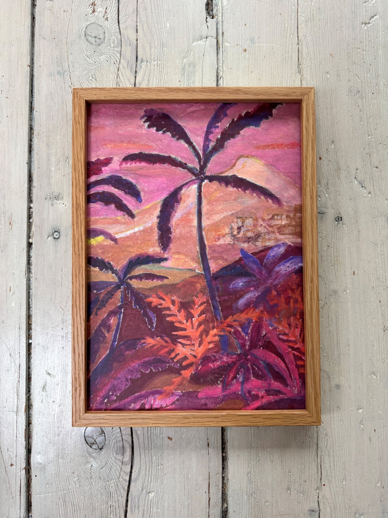 Wood display of multiple framed artworks including tropical painting, woman portrait, and dried flowers above white shelf