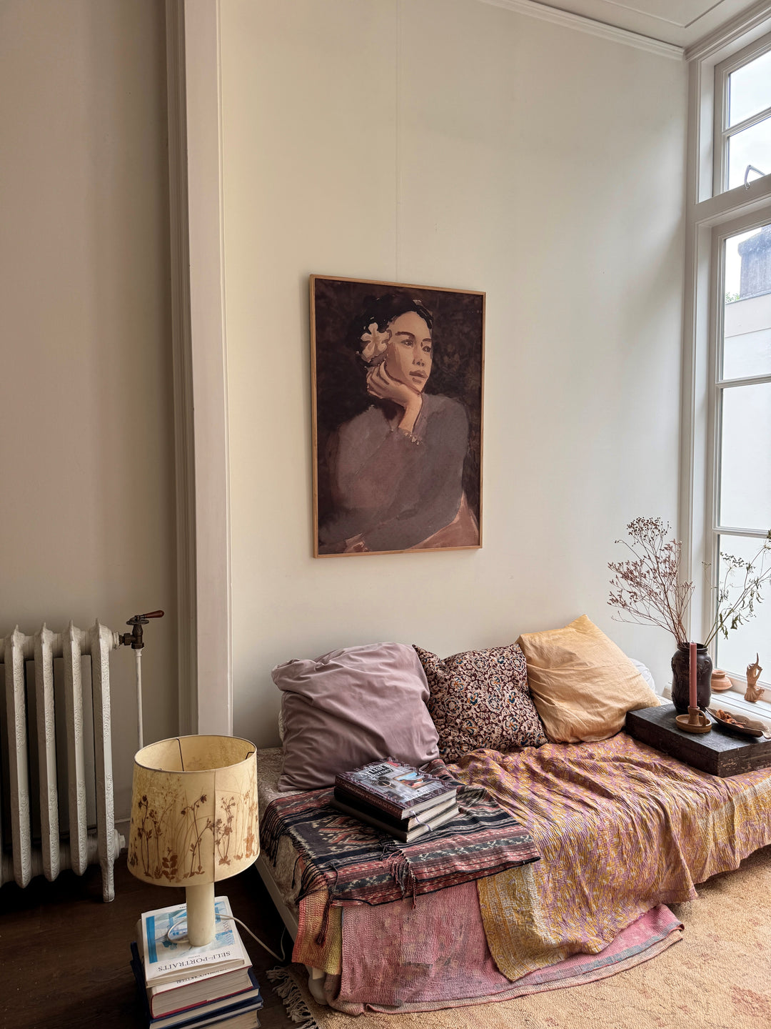 A pink and brown-toned painting of lady with a frangipani flower in hair against a white wall win a living room setting.