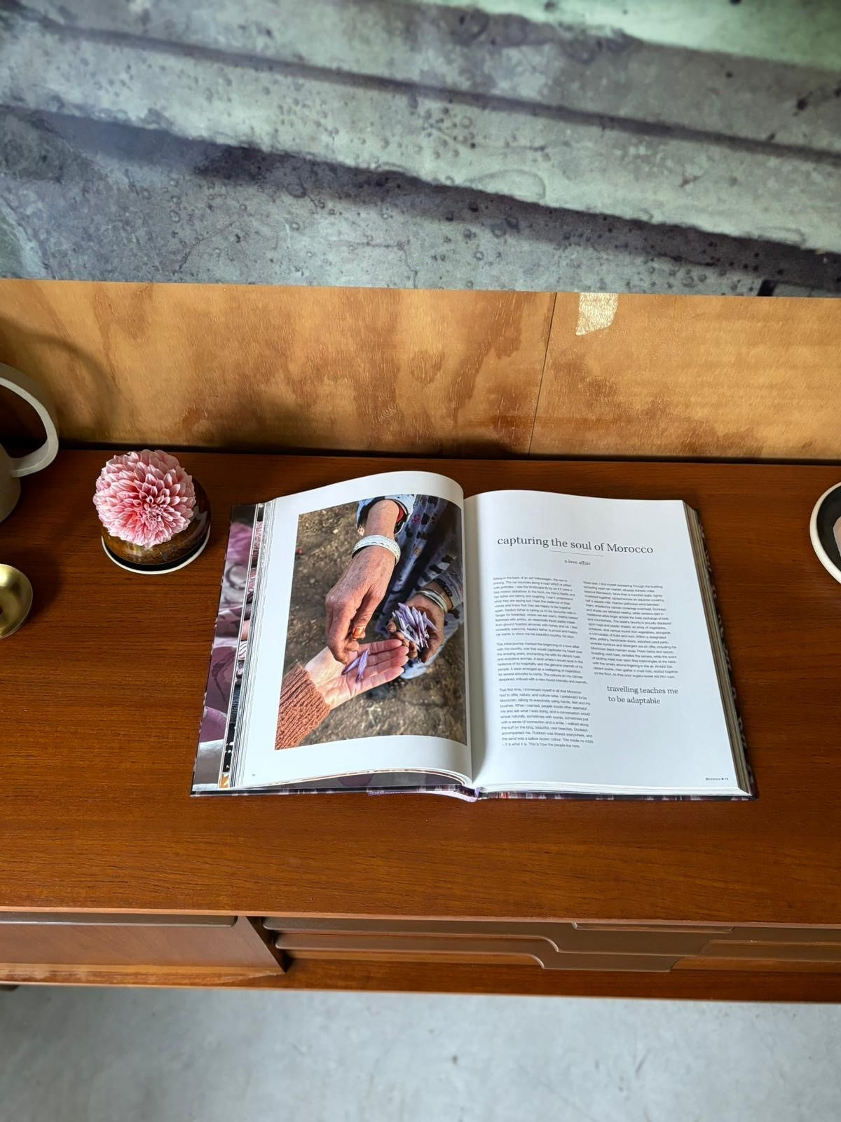 Open book showing photo and text titled "capturing the soul of Morocco" on wooden table with flower and brass candle.