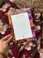 Hand holding floral gift card with space for recipient details and tinystories logo on purple patterned background