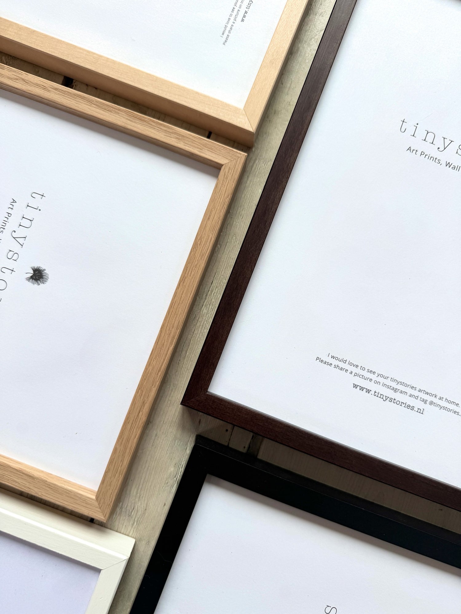 Close-up of four empty picture frames in natural wood, dark brown, black, and white colors on a wooden surface