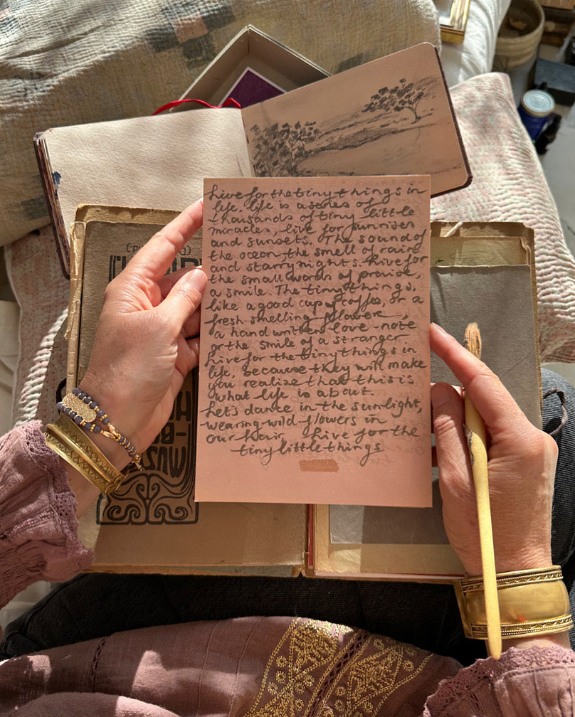 Hand holding pink handwritten note over a vintage book, soft natural light.