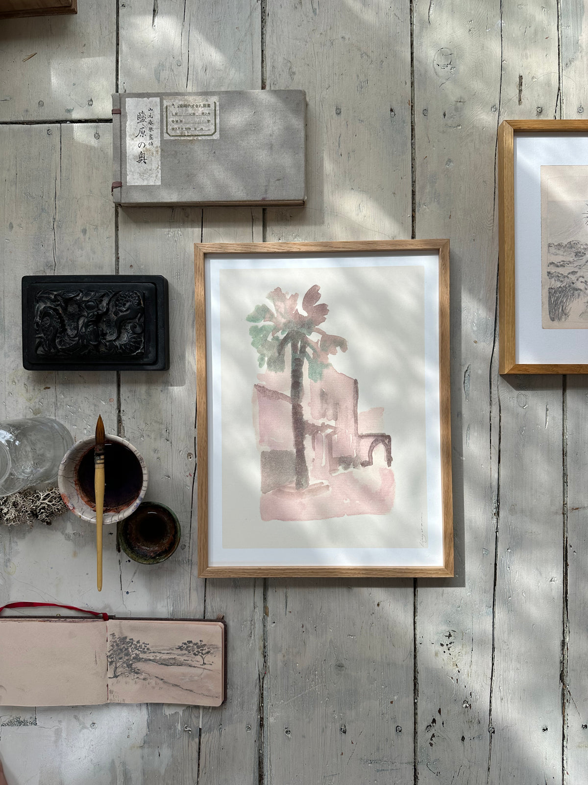 Close-up of framed palm tree watercolor painting with soft pastel colors and natural light on rustic wooden floor