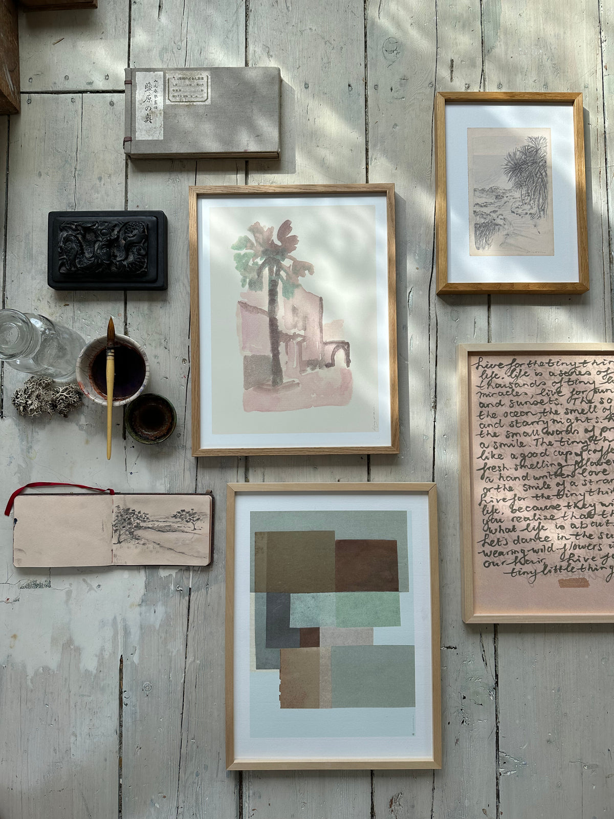 Collection of framed abstract, botanical, and figurative artworks including palm tree watercolor laid out on rustic wooden floor