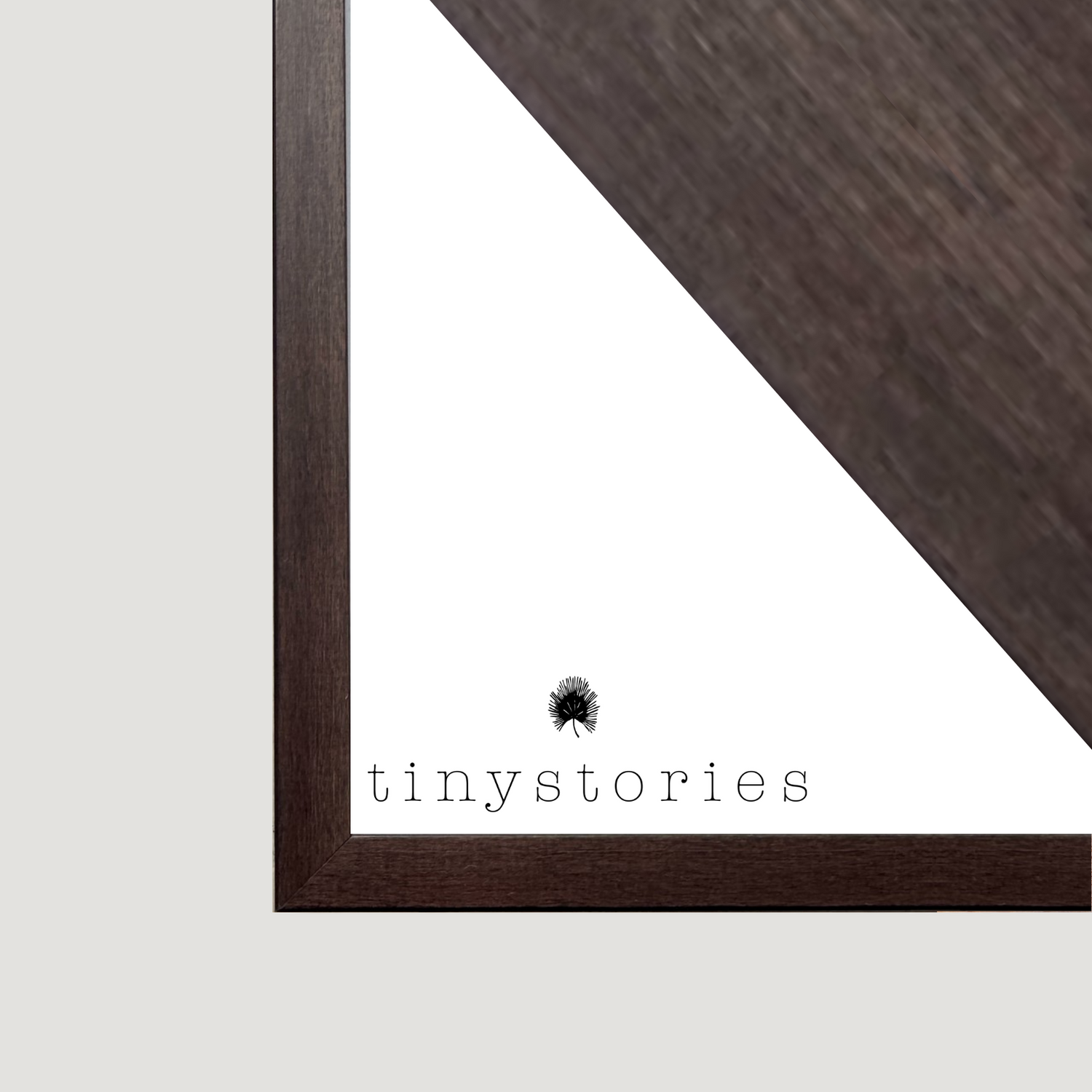 Close-up of dark wooden frame corner with TinyStories logo and small black leaf illustration on white background