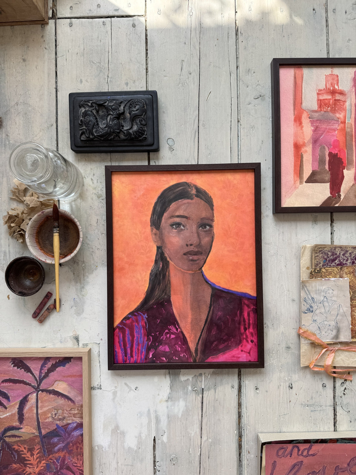 Framed watercolor portrait of woman with dark hair and purple jacket on rustic white wooden floor with paintbrush nearby