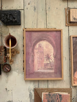 A framed painting laying on a wooden floor with art supplies sourrounding it.