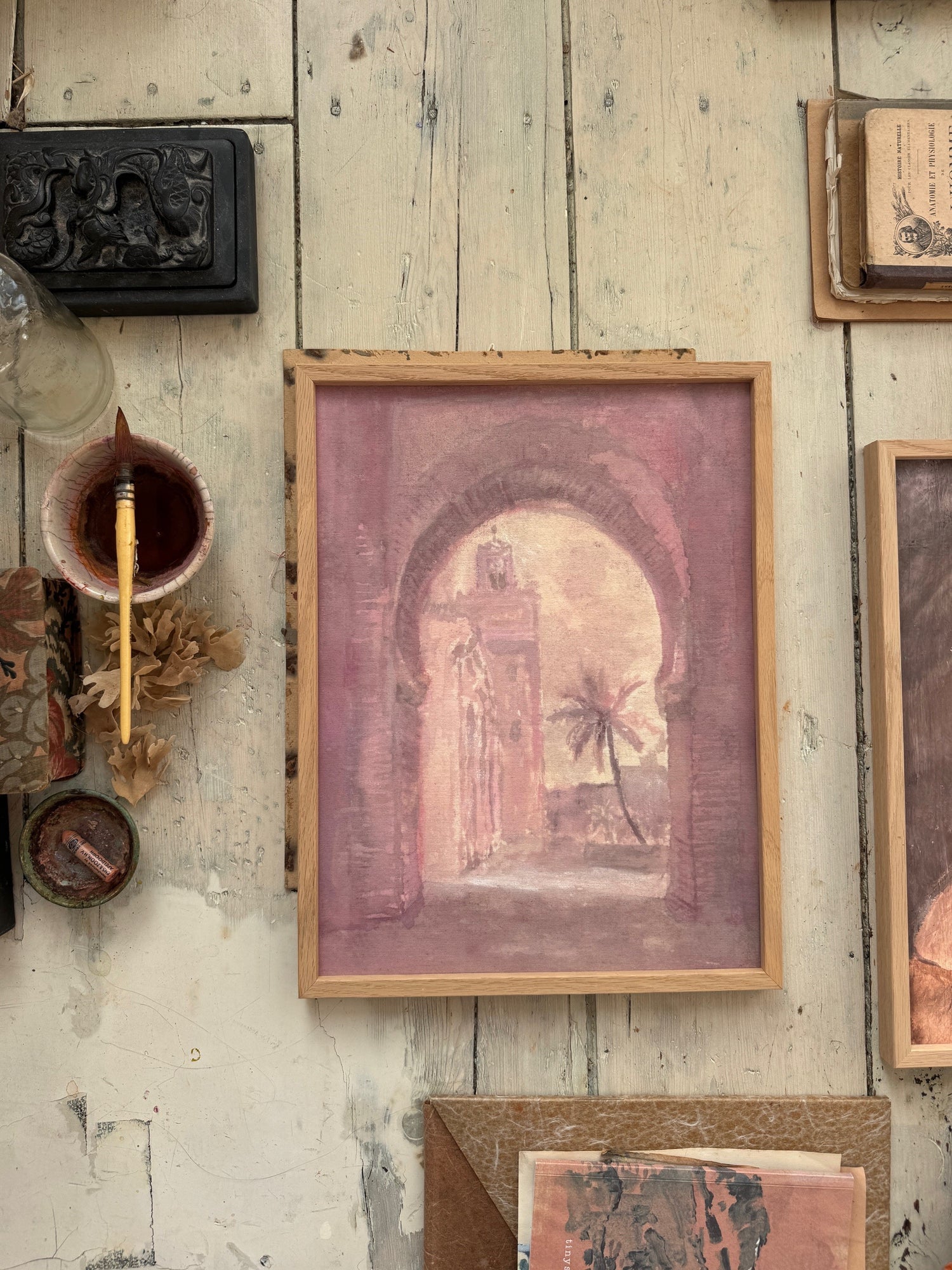 A framed painting laying on a wooden floor with art supplies sourrounding it.