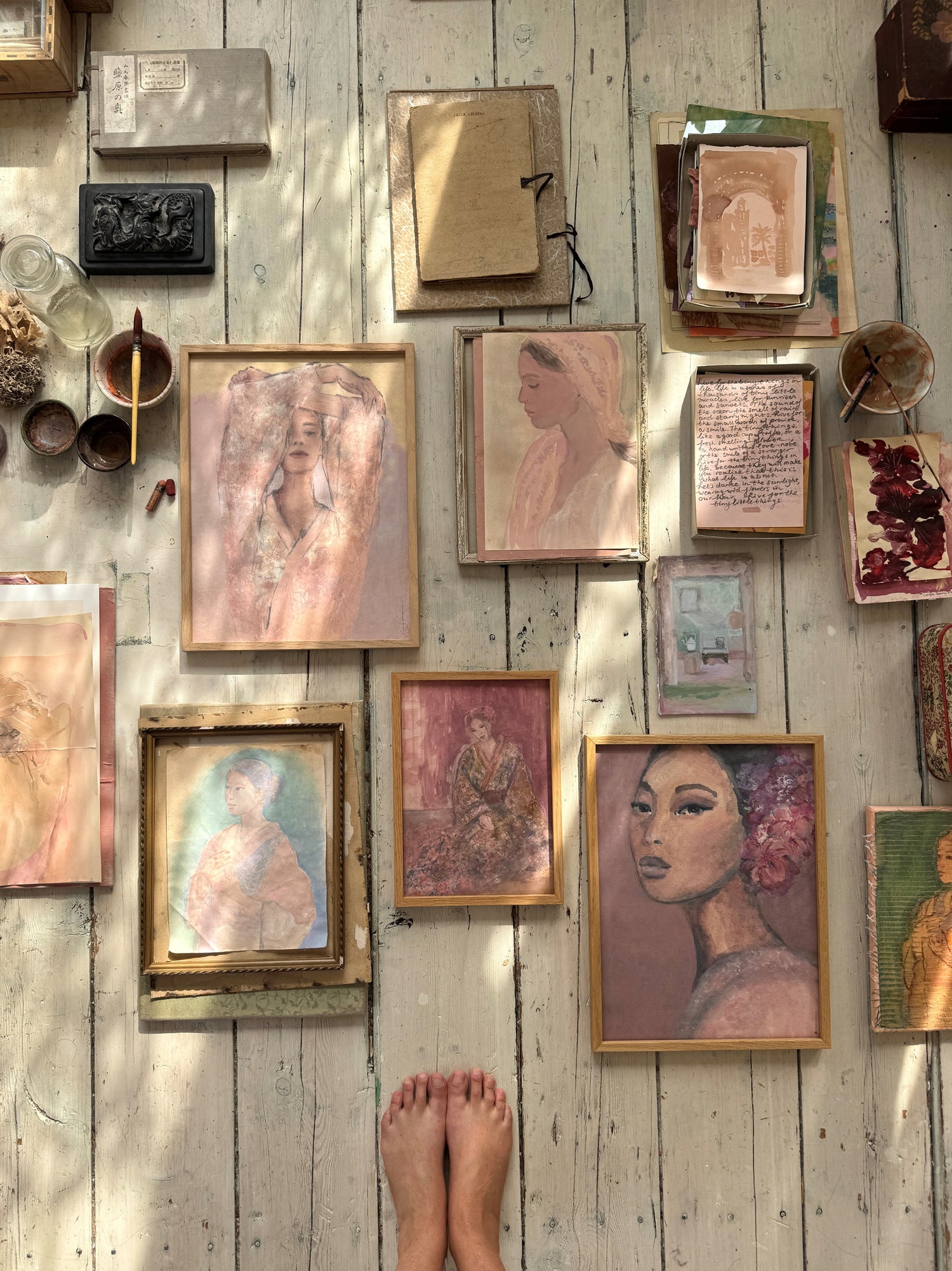 Collection of framed art prints laying on a wooden floor displaying female facec, womens portraits in shaded of soft pink.