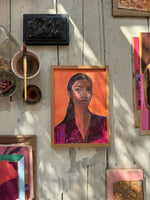 Top view of framed portrait of woman in purple jacket on white wooden floor with paintbrush and pastel chalks nearby