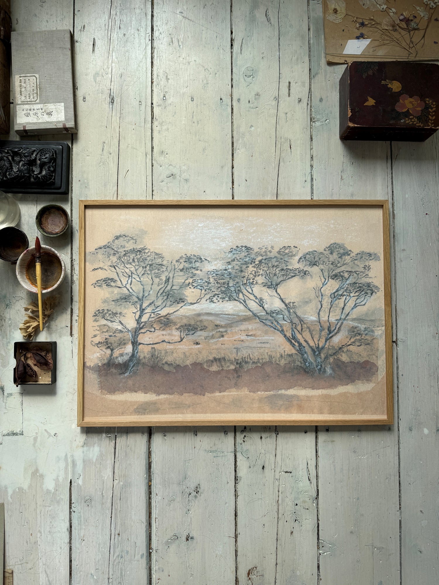 Horizontal framed landscape painting with bare trees on rustic wooden planks, sunlight highlights texture.

