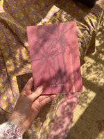 A hand of a woman golding a notebook in size DIN A5 showing a drawing of two palmtrees in shades of pink.