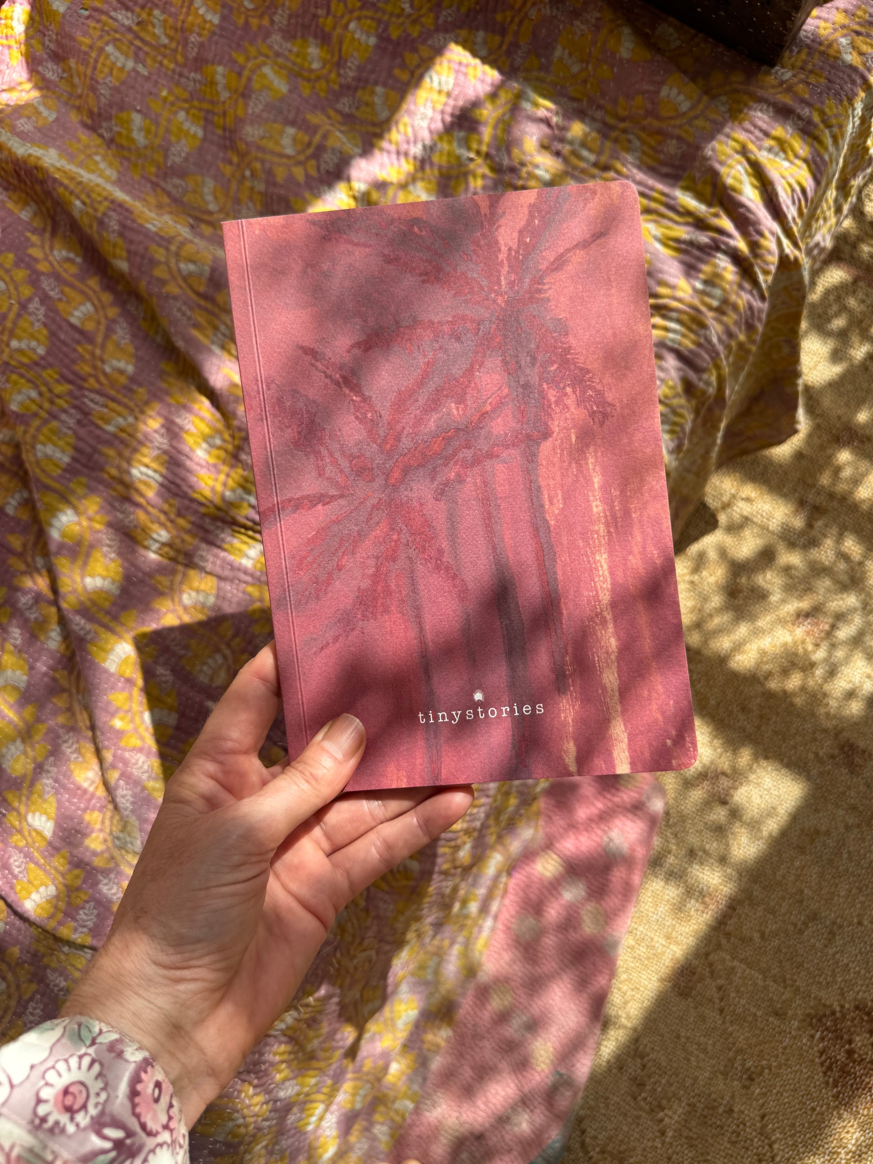 A hand of a woman golding a notebook in size DIN A5 showing a drawing of two palmtrees in shades of pink.
