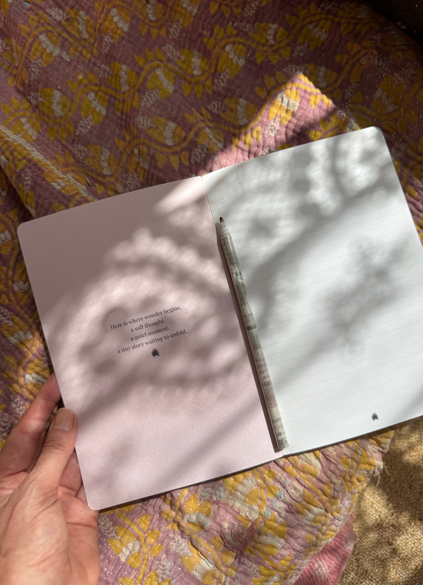 An open notebook in size DIN A5 laying on some colorful fabrich showing the inneer pages featuring an inspirational quote and fine dotted lines.