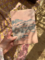 a hand holding a notebook in size DIN A5 showing an abstract landscape in soft colours